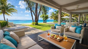 Un espace extérieur aménagé, abrité et doté de sièges, avec vue sur la plage et l’océan, comprenant des canapés et des fauteuils, ainsi qu’une table où sont servis des collations et des boissons.