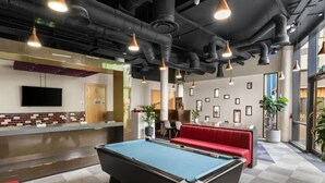 A pool table in a room with a checkered floor, a red sofa, and a television mounted on the wall. - Student Only Bronze Ensuite at Highbury  (London)