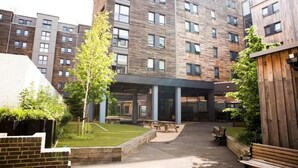 A multi-story building with a modern architectural design, featuring a courtyard with benches and a small lawn. - Student Only Bronze Ensuite at Highbury  (London)