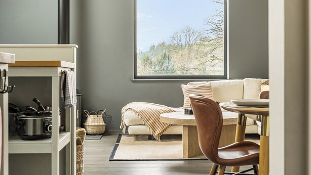 A modern living room with a large window, a sofa, a coffee table, and a dining area. - Grove Cottage (Kington)