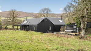 A black metal building with a sloped roof, a small deck, and a chimney. - Grove Cottage (Kington)