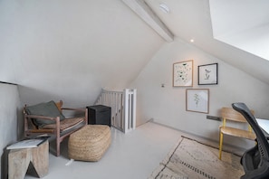 A loft-style room with a sloped ceiling, a wooden chair, a small table, a woven ottoman, and framed botanical prints on the wall. - Grove Cottage (Kington)