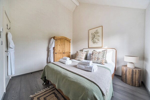 A bedroom with a bed, a wooden wardrobe, a framed botanical print, a bedside lamp, and a rug. - Grove Cottage (Kington)