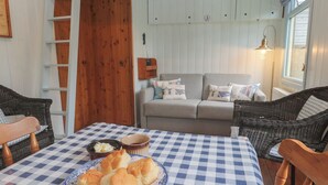 A cozy room with a checkered tablecloth, a plate of biscuits, a wicker chair, a sofa with patterned cushions, and a wooden door. - Pleasans (Hayle)