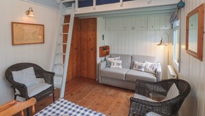 A cozy room with a loft bed, a sofa, wicker chairs, a table with a checkered tablecloth, and a wooden floor. - Pleasans (Hayle)