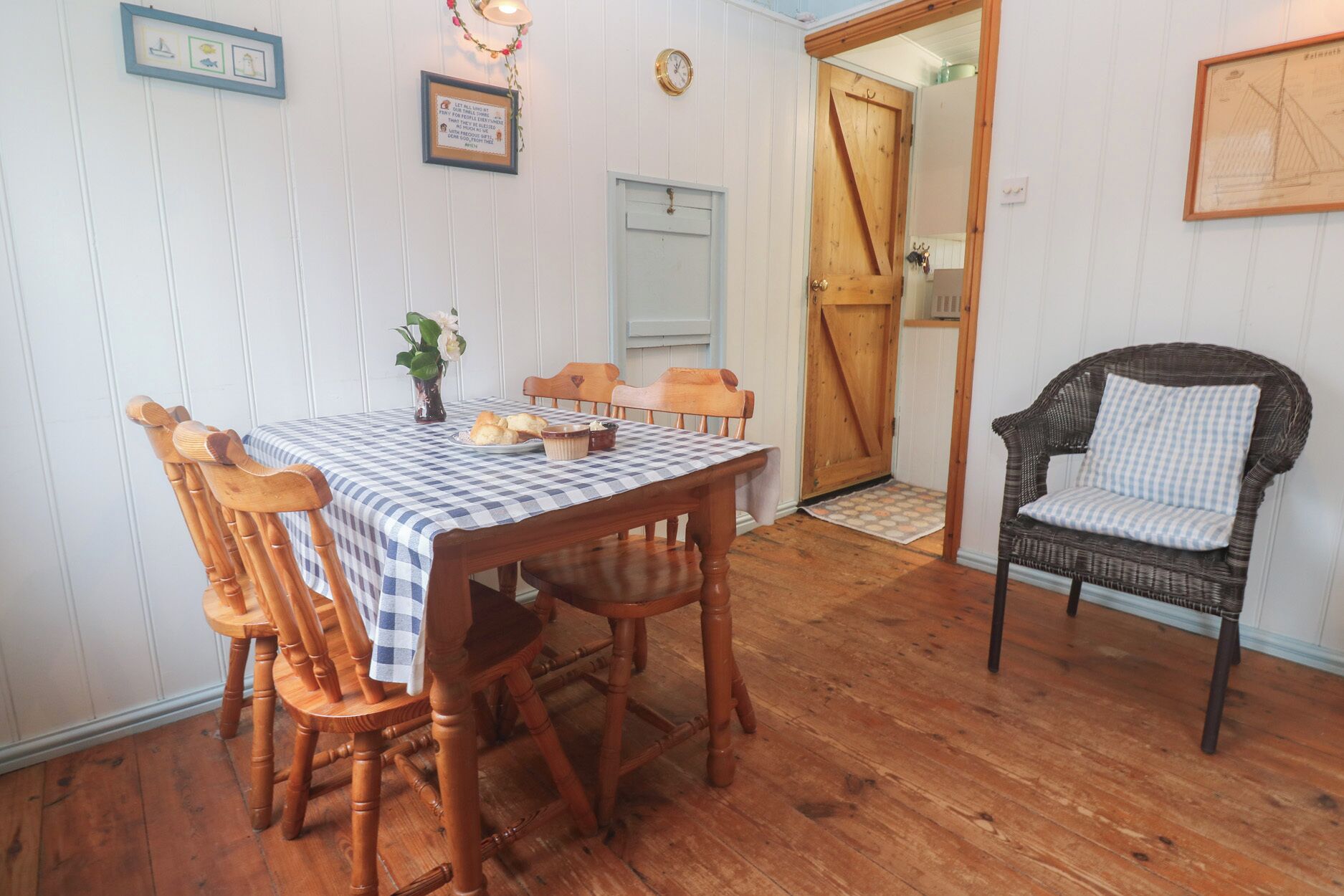 Un comedor con mantel a cuadros, sillas de madera, un sofá de mimbre y una puerta que da a otra habitación.