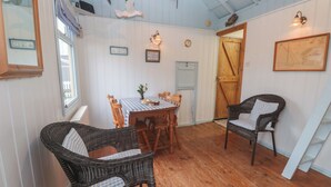 A cozy room with a wooden table and chairs, a wicker chair, a wooden door, and wall-mounted lights. - Pleasans (Hayle)