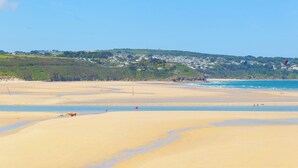 A wide sandy beach with a clear view of a hillside with houses in the background. - Pleasans (Hayle)