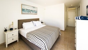 A bedroom with a bed, bedside tables, a nightstand, a painting, and a bathroom with a towel rack. - Stylish Carvoeiro Villa | Heated Private Pool | Sea Views | Roof Terrace (Carvoeiro)