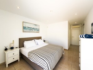 A bedroom with a bed, bedside tables, a nightstand, a painting, and a bathroom with a towel rack. - Stylish Carvoeiro Villa | Heated Private Pool | Sea Views | Roof Terrace (Carvoeiro)
