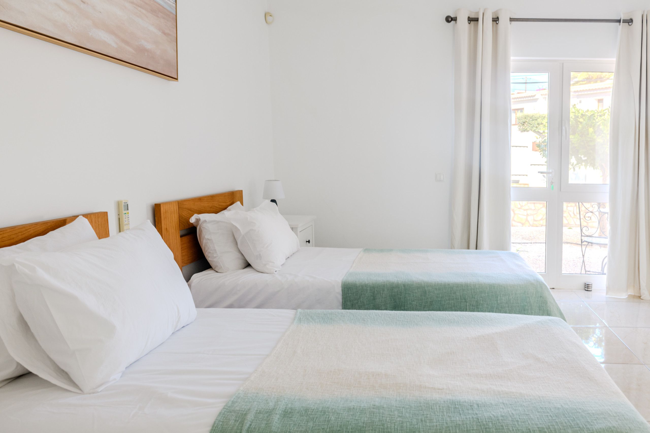 Quarto de hotel com duas camas, mesa de cabeceira com abajur, janela com cortinas e vista para o exterior.