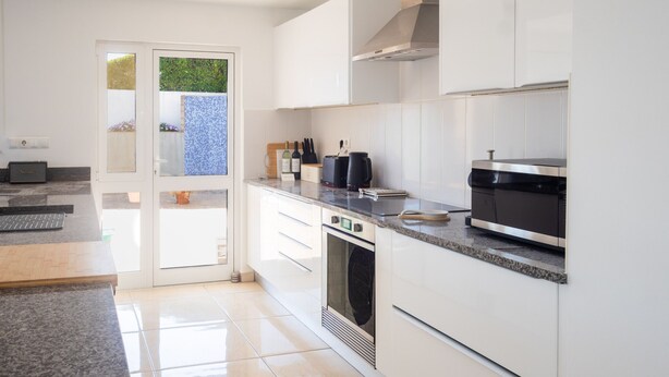 A modern kitchen with white cabinetry, a built-in oven, and a coffee maker on the countertop. - Stylish Carvoeiro Villa | Heated Private Pool | Sea Views | Roof Terrace (Carvoeiro)