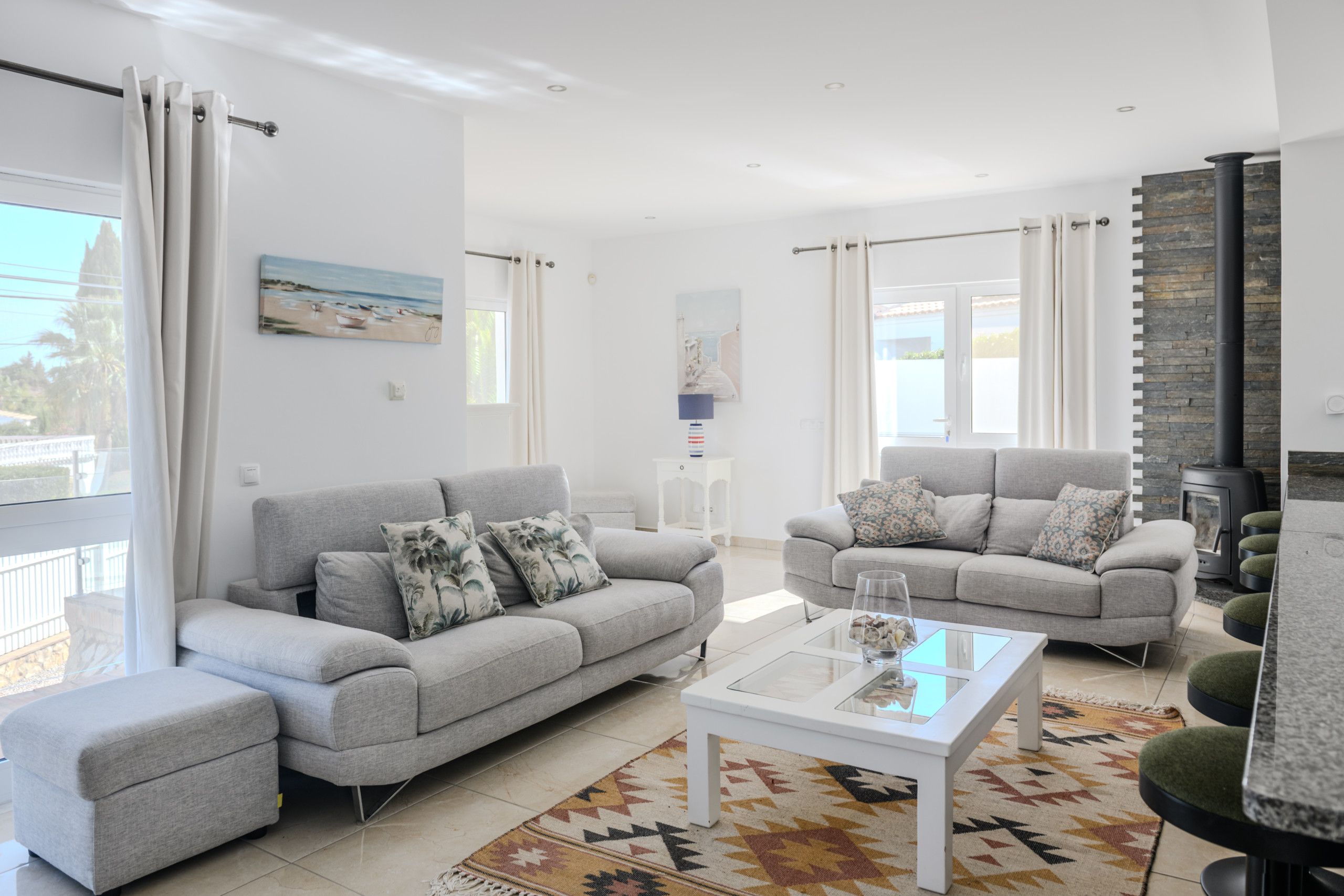 A modern living room with two grey sofas, a glass coffee table, and a patterned rug.
