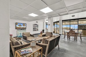 A spacious lounge area with a large window, a bookshelf, and a seating arrangement. - Waterpointe II 701 l Oceanfront l 3BR l Pools (North Myrtle Beach)