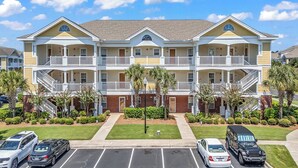A multi-story hotel with balconies, a parking lot, and well-maintained landscaping. - The Havens at Barefoot Landing l 2BR l Pool (North Myrtle Beach)