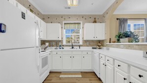 A kitchen with white cabinets, a window with a view, and a wooden floor. - The Havens at Barefoot Landing l 2BR l Pool (North Myrtle Beach)