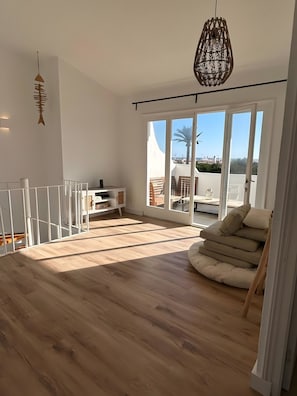 Een ruime kamer met een houten vloer, een witte leuning, een groot raam met uitzicht en een hanglamp.