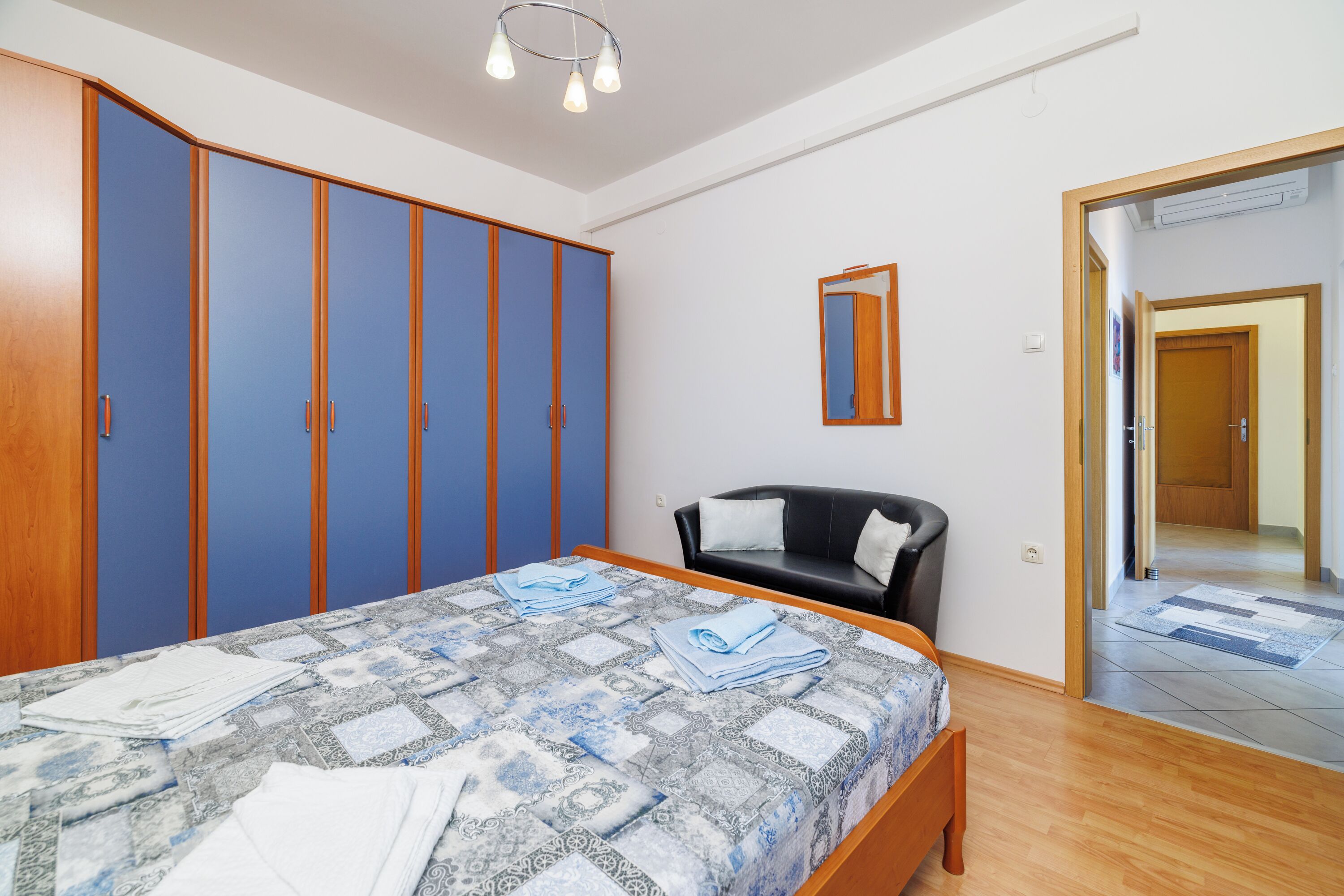 A bedroom with a bed, a black chair, a wardrobe, and a mirror.
