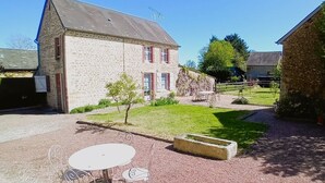 Un bâtiment en pierre avec une petite pelouse et une table entourée de chaises.