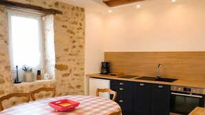 Une cuisine avec une nappe à carreaux, des chaises en bois, un évier, des placards et un lave-vaisselle.