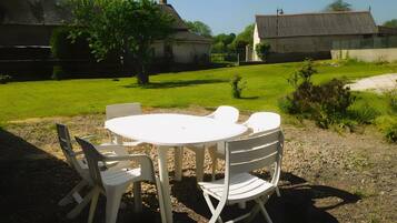 A round outdoor table with four chairs, surrounded by gravel and grass, with buildings in the background.