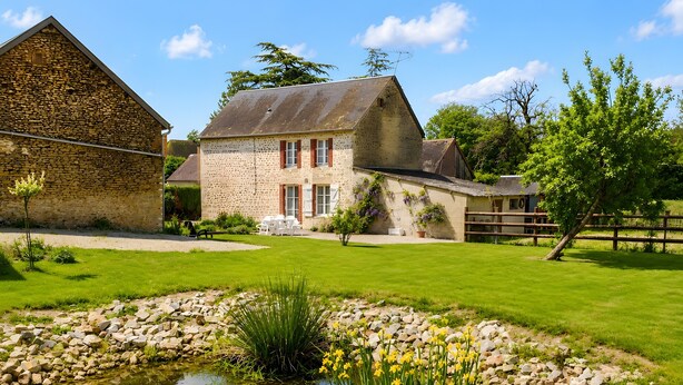 Un bâtiment en pierre avec un bassin, entouré d’une pelouse bien entretenue et d’une clôture en bois.