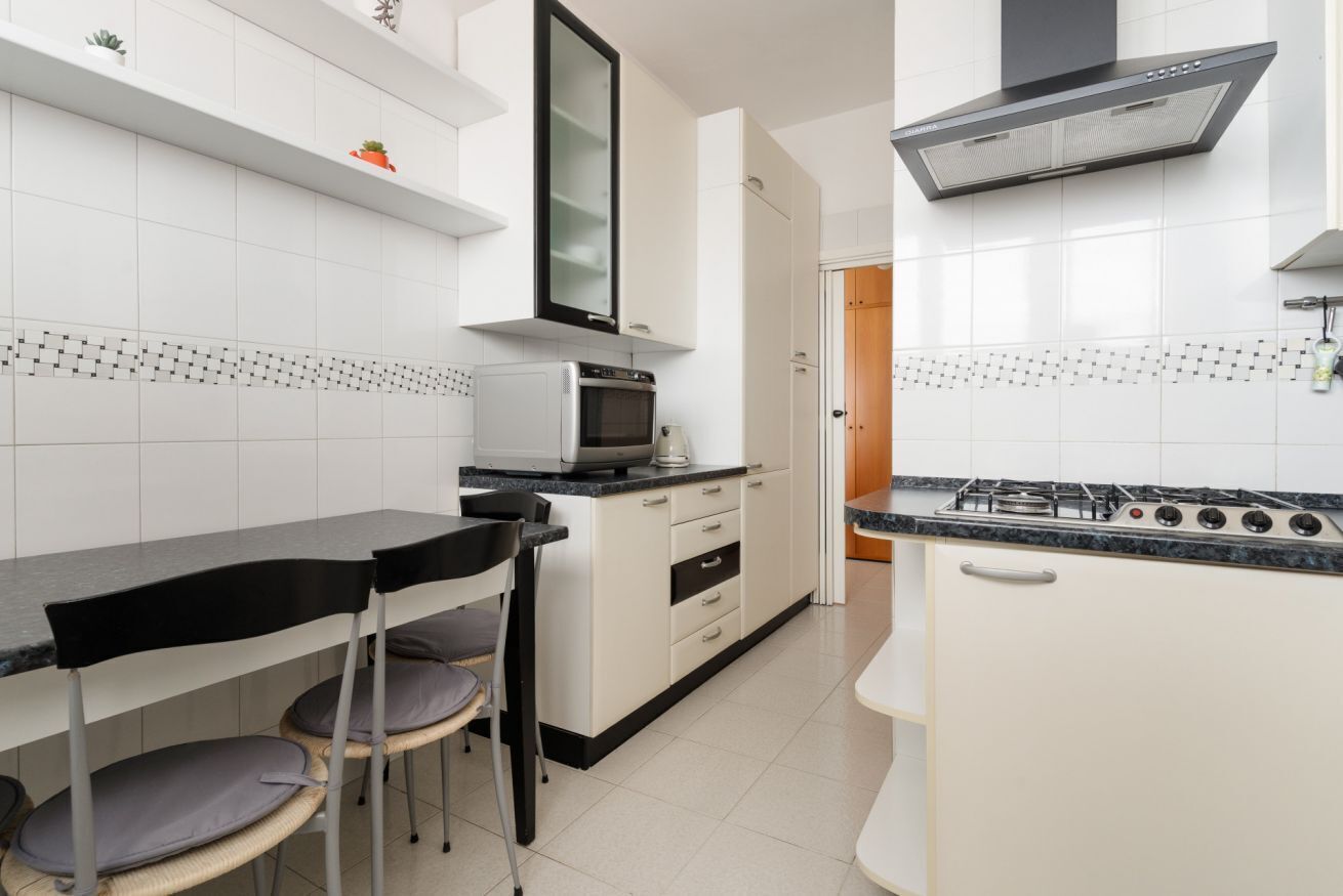 Une cuisine avec des meubles blancs, un four à micro-ondes, une cuisinière et un coin repas avec des chaises.