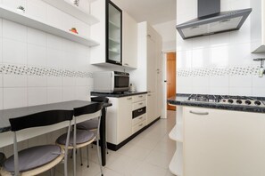 A kitchen with white cabinets, a microwave, a stove, and a dining area with chairs. - GuestHost - Cozy 58m2 apartment, perfect for 4 people, located on the fifth floor of a building with lift.The accommodation is located in the Crescenzago area, well connected thanks to the Crescenzago metro stop (M2-Verde) and buses #44, #54, #51 and # (Milan)
