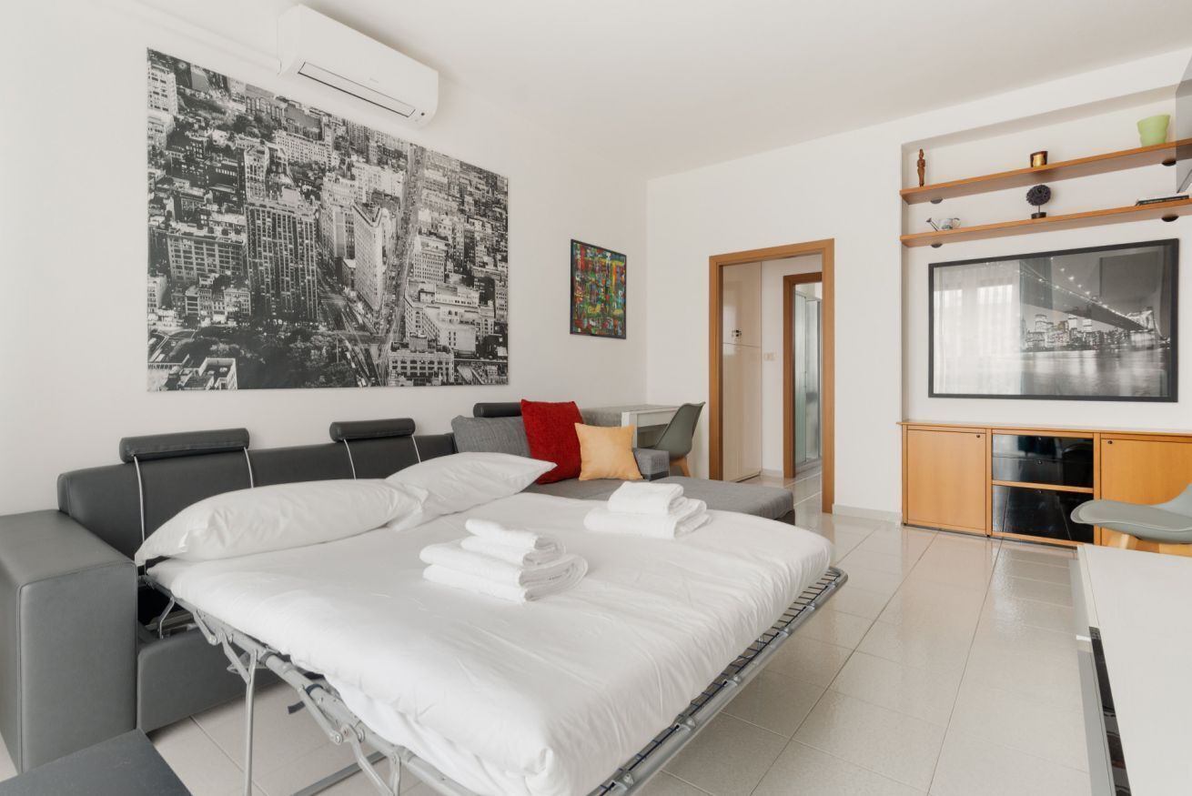 A modern hotel room with a bed, a sofa, a TV, and artwork on the walls.