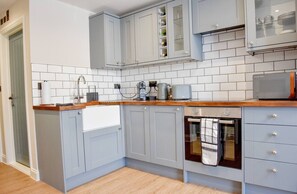 Una cocina con gabinetes grises, encimera de madera, horno empotrado y salpicadero de azulejos.