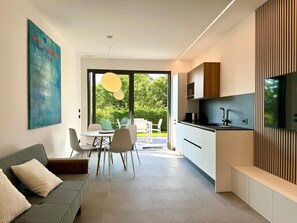 Eine moderne Küche mit Einbauofen, eine Essecke mit Tisch und Stühlen sowie ein großes Fenster mit Blick ins Freie.