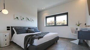 A modern bedroom with a bed, bedside tables, a window, and artwork on the wall. - Aria Art Suite   Lake View Terrace and Private Hot Tub (BARDOLINO)