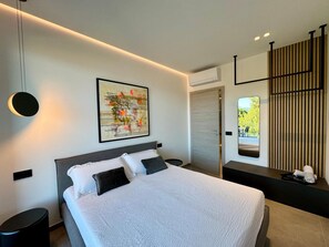 Ein modernes Schlafzimmer mit einem großen Bett, einem Wandbild, einem Nachttisch und einem Fenster mit Blick.