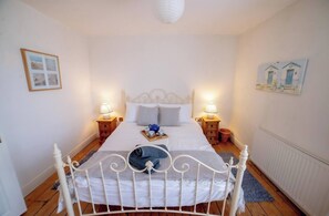 Ein Schlafzimmer mit einem weißen Bett, zwei Nachttischen mit Lampen, einem gerahmten Bild an der Wand und einer Heizung.