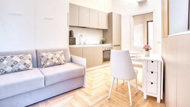 Een moderne woonkamer met een bank, een fauteuil, een klein bureau en een keukenhoek.