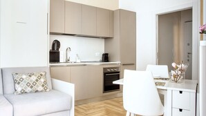 Een compacte keuken met een ingebouwde oven, een eethoek met een witte tafel en stoel, en een bank met een gestreept kussen.