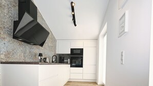 Une cuisine étroite avec des meubles blancs, une hotte noire et un plancher en bois.