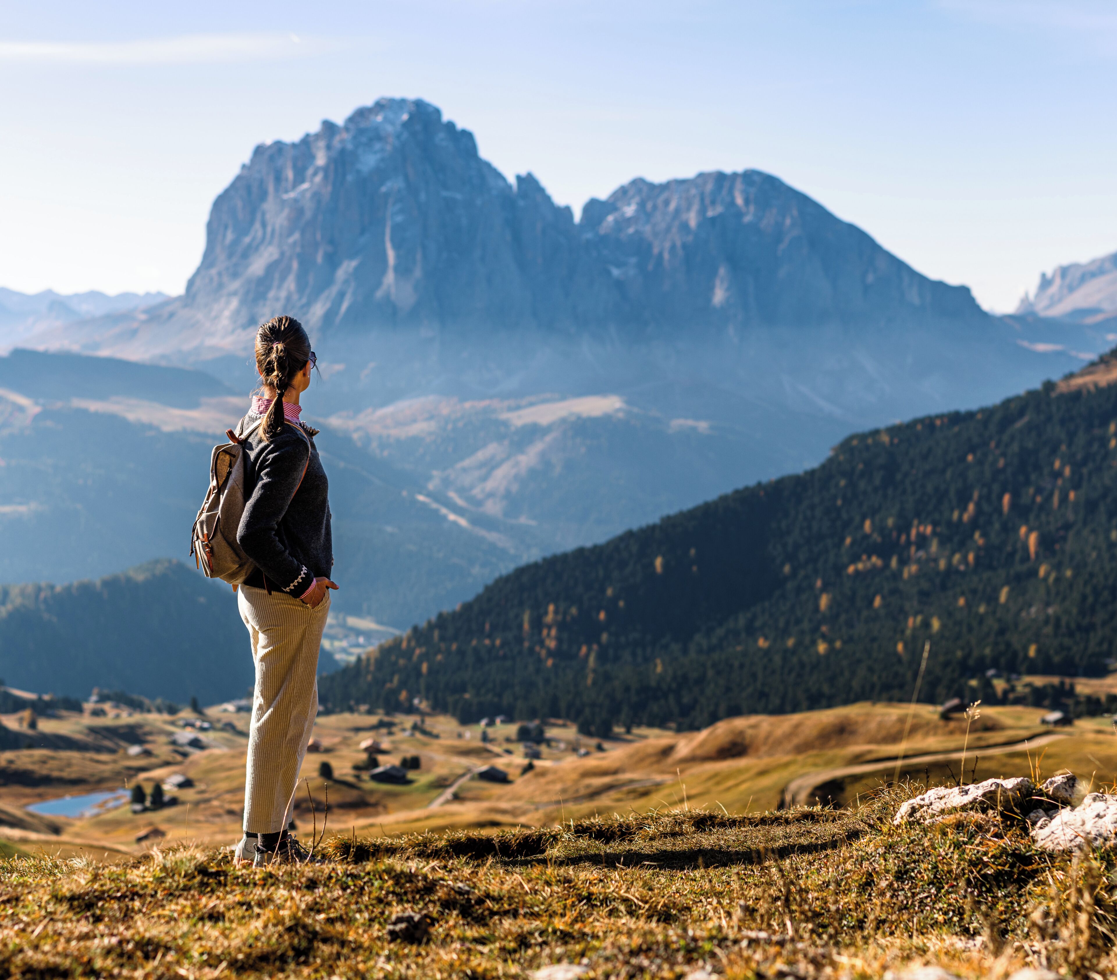 Eine Person steht auf einem grasbewachsen Hügel, im Hintergrund eine gebirgige Landschaft.