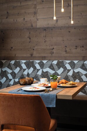 Ein Essbereich mit Holzwand, gemustertem Tapeten und einem Tisch mit Frühstücksgebäck, beleuchtet von hängenden Pendelleuchten.