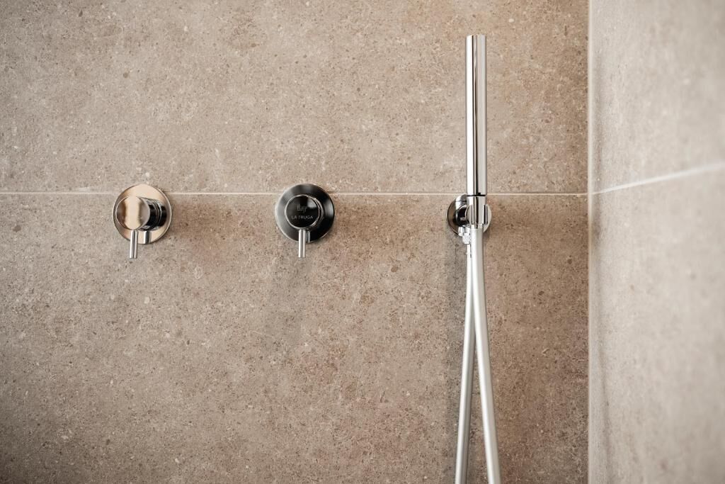 Une douche avec un robinet chromé et un bouton de commande sur un mur carrelé.