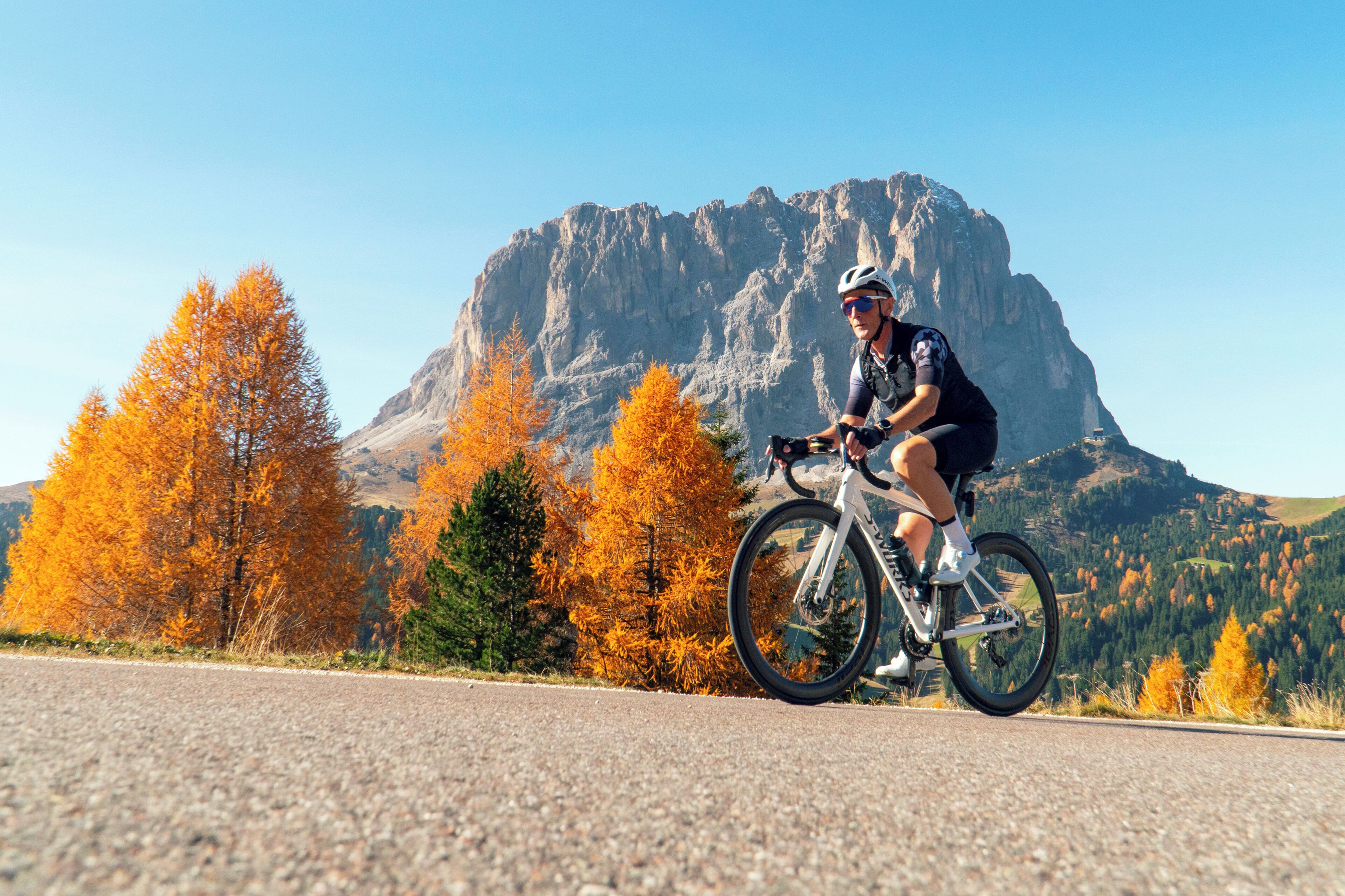 A person riding a bicycle on a road with autumn trees and a mountain in the background.