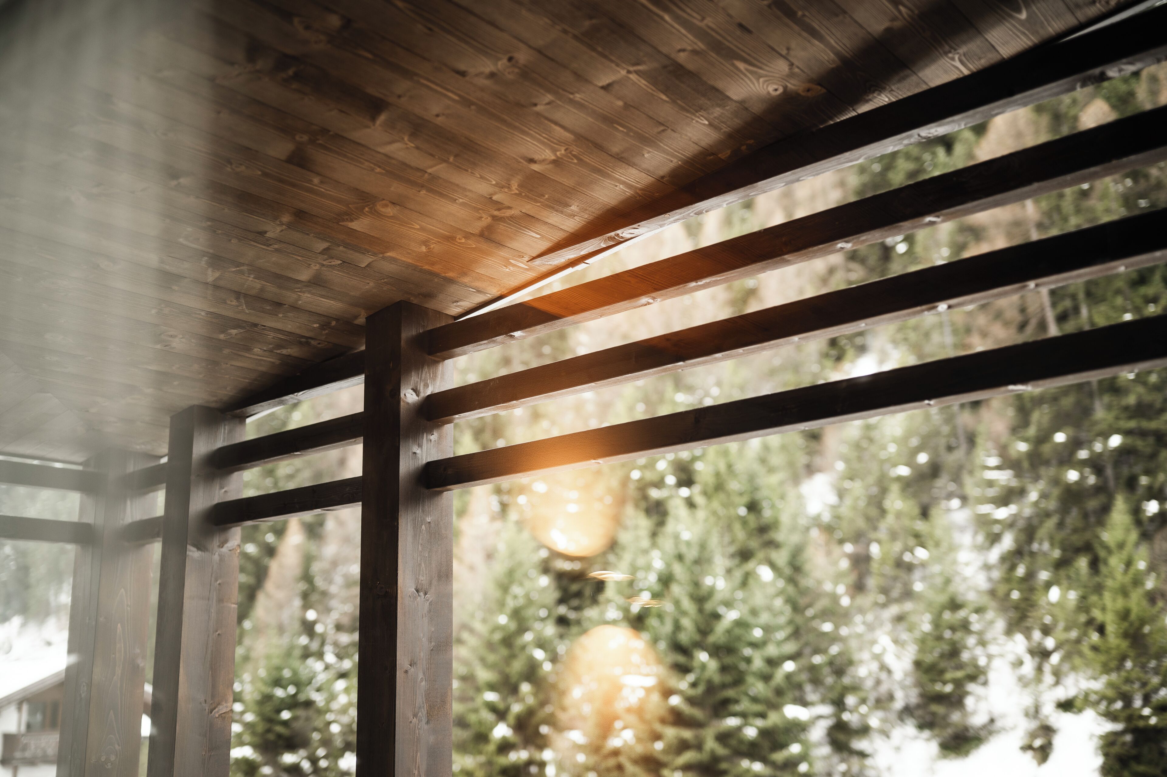A wooden ceiling structure with beams and a view of trees through a window.