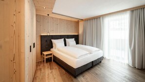 A modern bedroom with a wooden floor, a large bed, a nightstand, and a window with curtains. - Hotel La Truga (Selva di Val Gardena)
