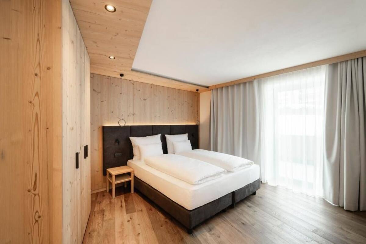 Een moderne slaapkamer met een houten vloer, een groot bed, een nachtkastje en een raam met gordijnen.