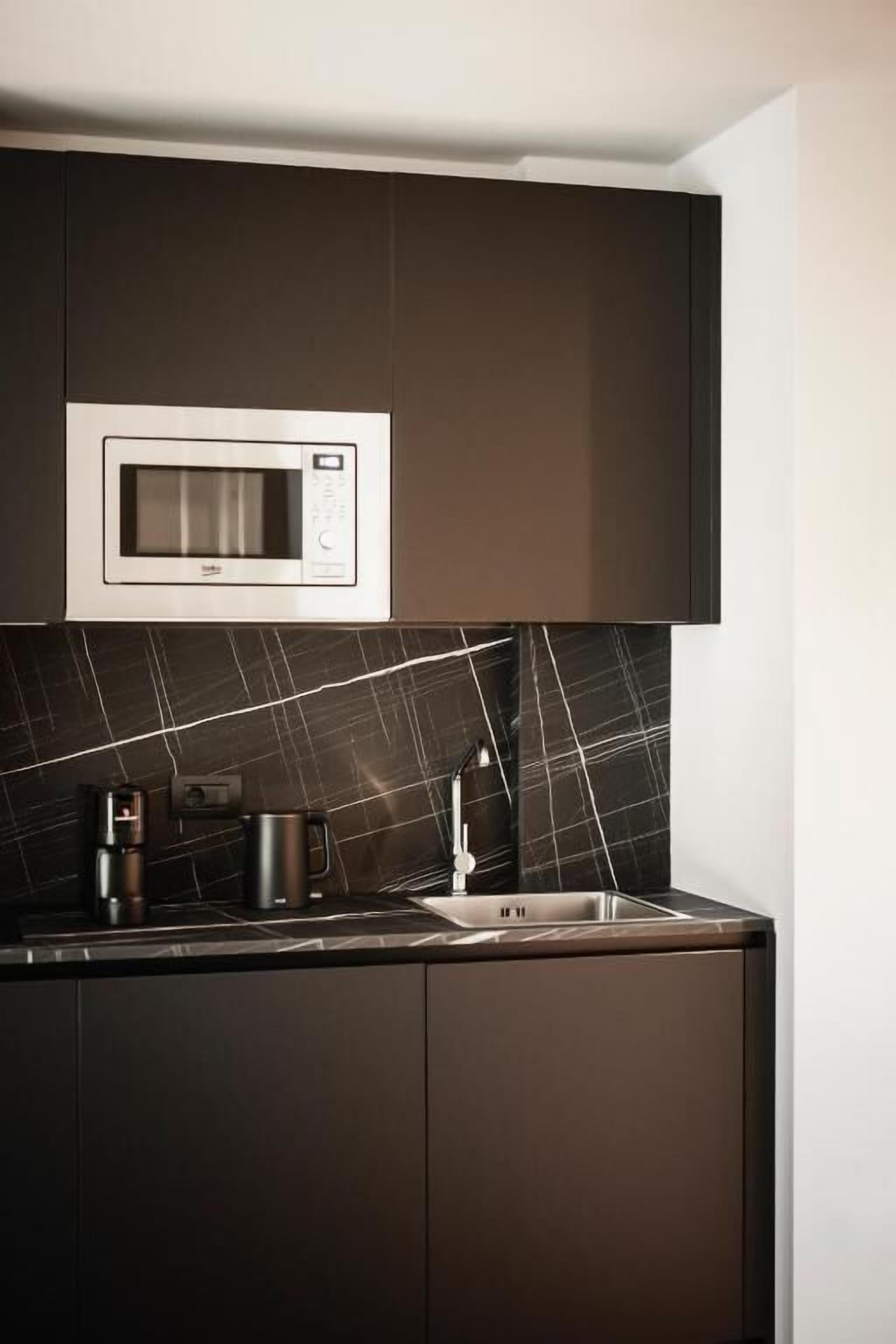 A modern kitchen with dark cabinetry, a built-in microwave, a coffee maker, and a sink.