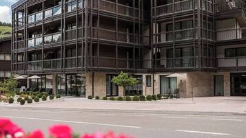 A modern multi-story building with balconies, large windows, and a landscaped area with flowers.