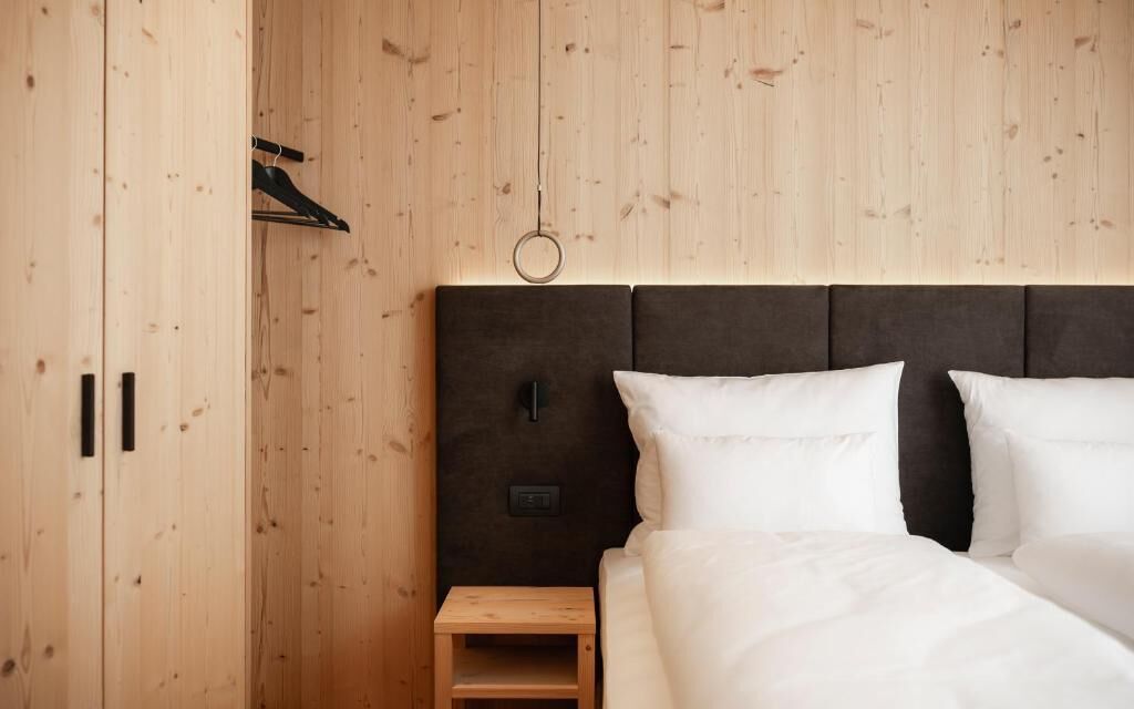 A wooden-paneled room with a bed, a small wooden nightstand, and a wall-mounted light fixture.