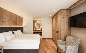 Ein modernes Schlafzimmer mit einem großen Bett, einem Fernseher, einem gemusterten Sessel und einem Holzschrank.