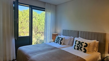 Una habitación de hotel con una cama, una mesita de noche, una lámpara y una ventana con cortinas.