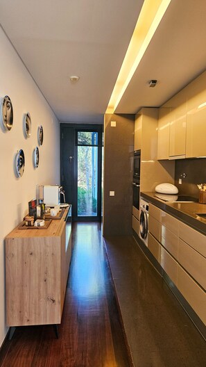 Una cocina moderna con horno empotrado, cafetera y vistas a un jardín a través de una puerta.